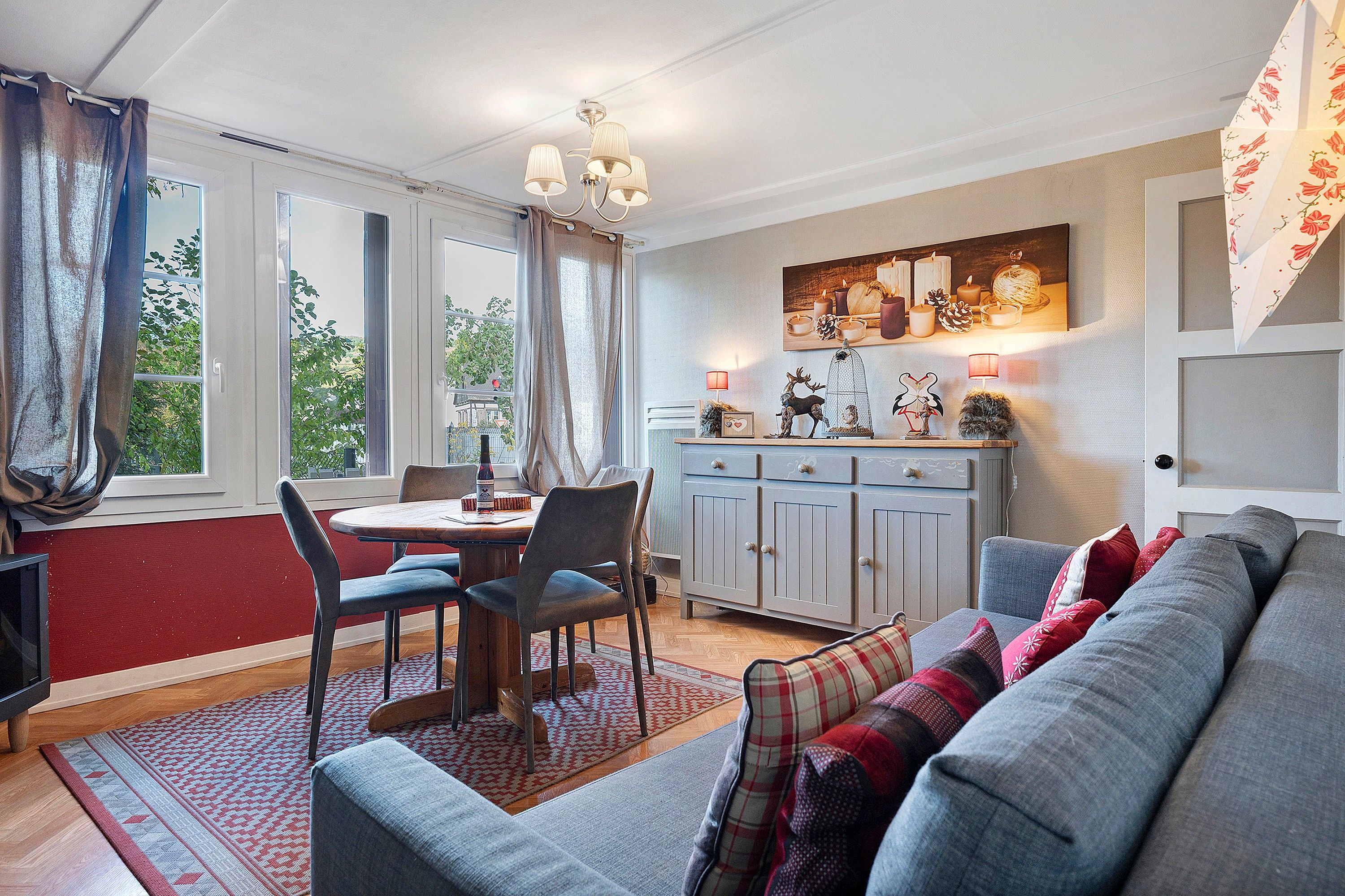 A cozy living room with a sofa, a dining table with chairs, a kitchen area with cabinets, and a large window with curtains.