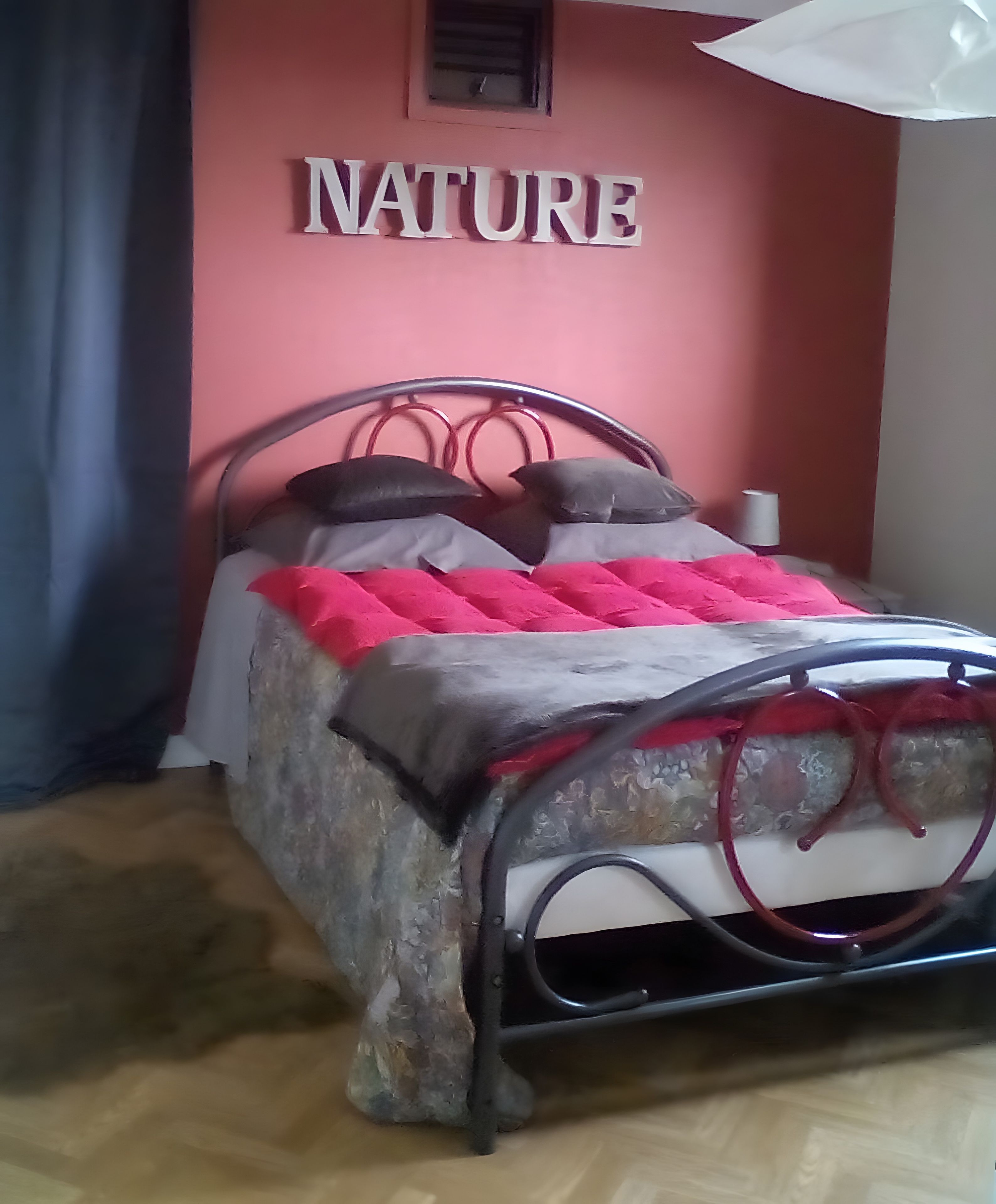 Un lit avec un cadre en métal et un mur rose sur lequel on peut voir le mot « NATURE » en arrière-plan.
