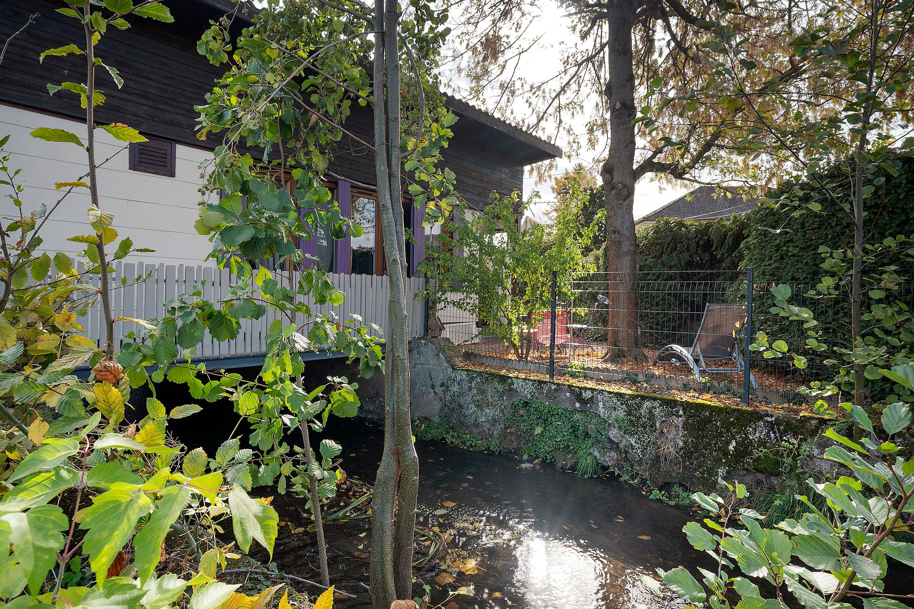 Un quartier résidentiel avec une maison blanche, une clôture en bois et un petit ruisseau.