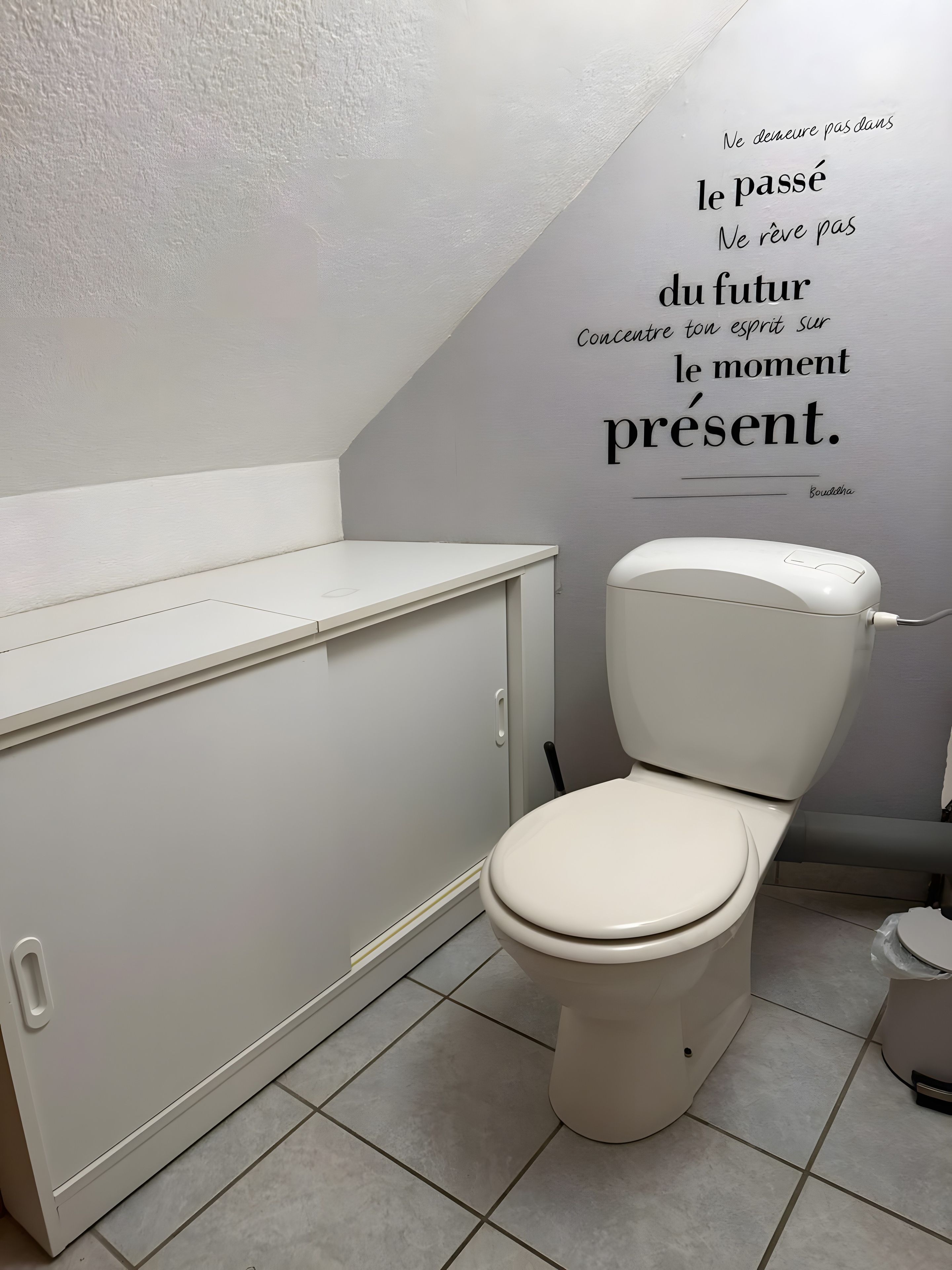 Une salle de bain avec des toilettes, un meuble et un mur orné d’une citation inspirante.