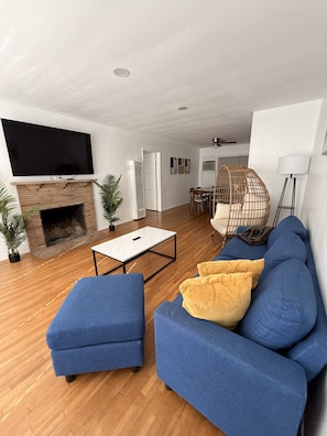 Ein modernes Wohnzimmer mit einem Flachbildfernseher über einem Kamin aus Ziegelsteinen, einem blauen Sofagarnitur, einem weißen Couchtisch und einem Korbstuhl.
