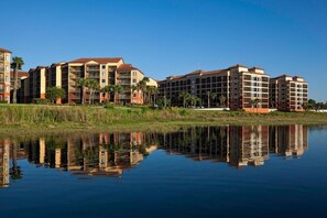 A multi-story hotel with balconies, a reflection in the water, and palm trees in the foreground. - 2-bedroom villa in Orlando Florida " The perfect Disney Family Fun get away" (Orlando)
