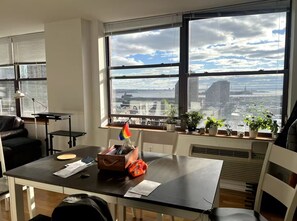 A modern office space with a large window offering a city view, a desk with papers and a small plant, and a leather couch. - Cozy 1-bedroom apartment in gorgeous Jersey City with AC and gym access (Jersey City)