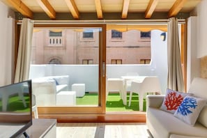 A modern room with a sliding glass door leading to an outdoor seating area with white furniture and a green lawn. - Urban Suites Palma (Palma)
