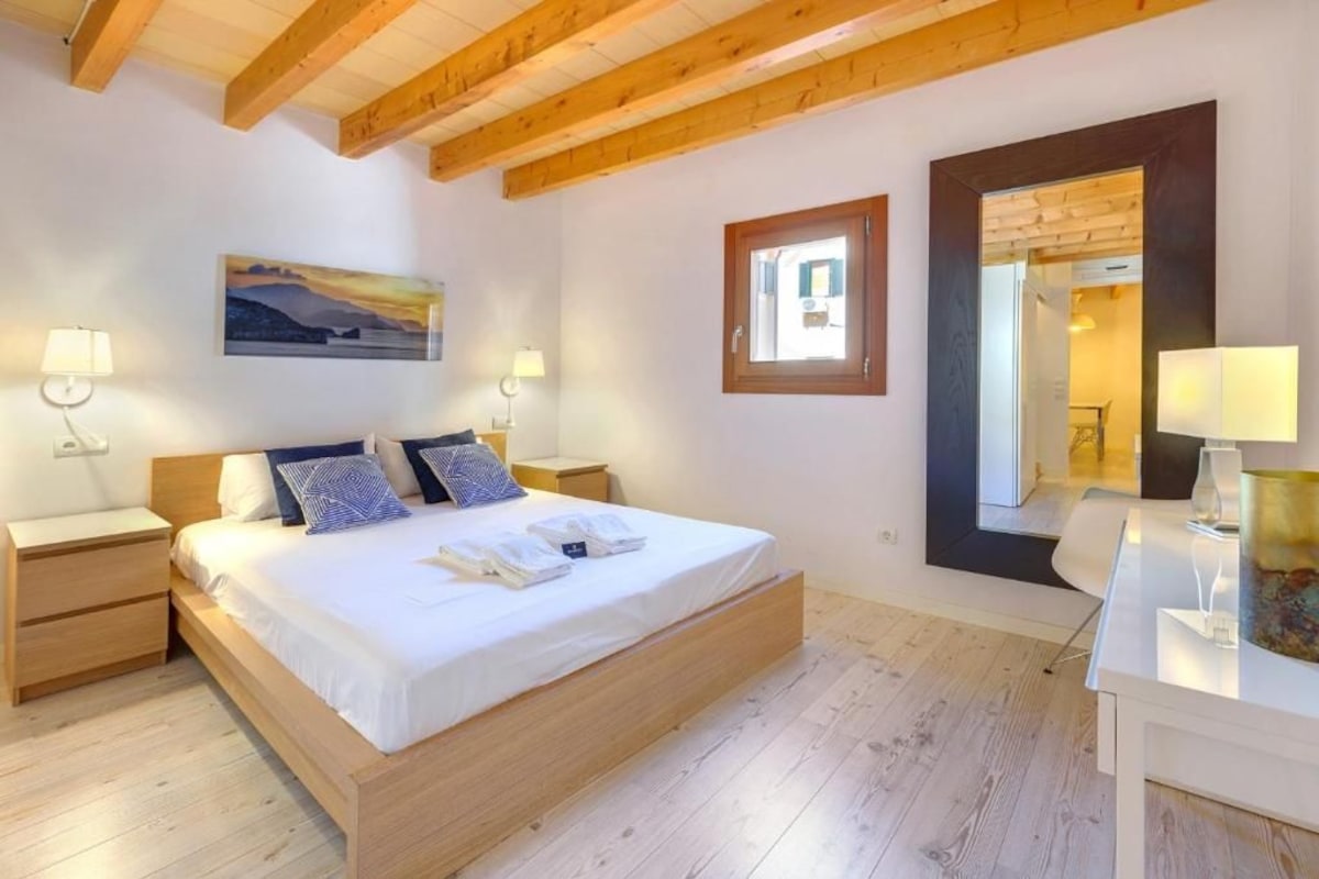 A bedroom with a wooden bed, bedside tables, a nightstand, a mirror, and a painting on the wall.