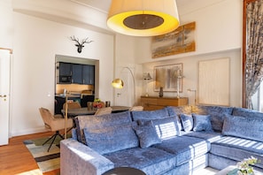 Una sala de estar con un sofá azul, una mesa de comedor con sillas, una zona de cocina y una cabeza de venado montada en la pared.