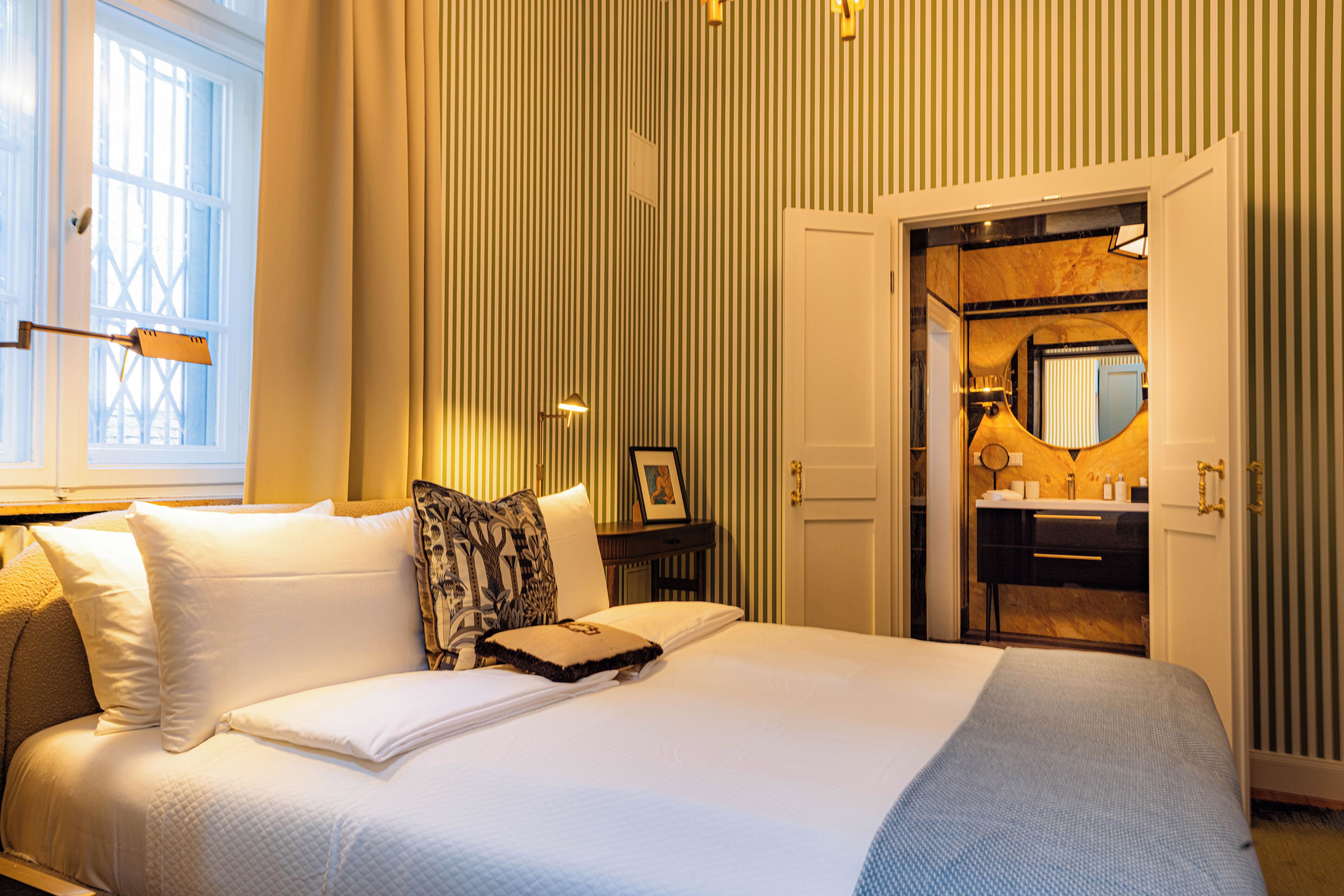 A hotel room with a large bed, a bedside table, a mirror, and a door leading to a bathroom.