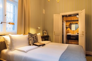 Una habitación de hotel con una cama grande, una mesita de noche, un espejo y una puerta que da a un baño.