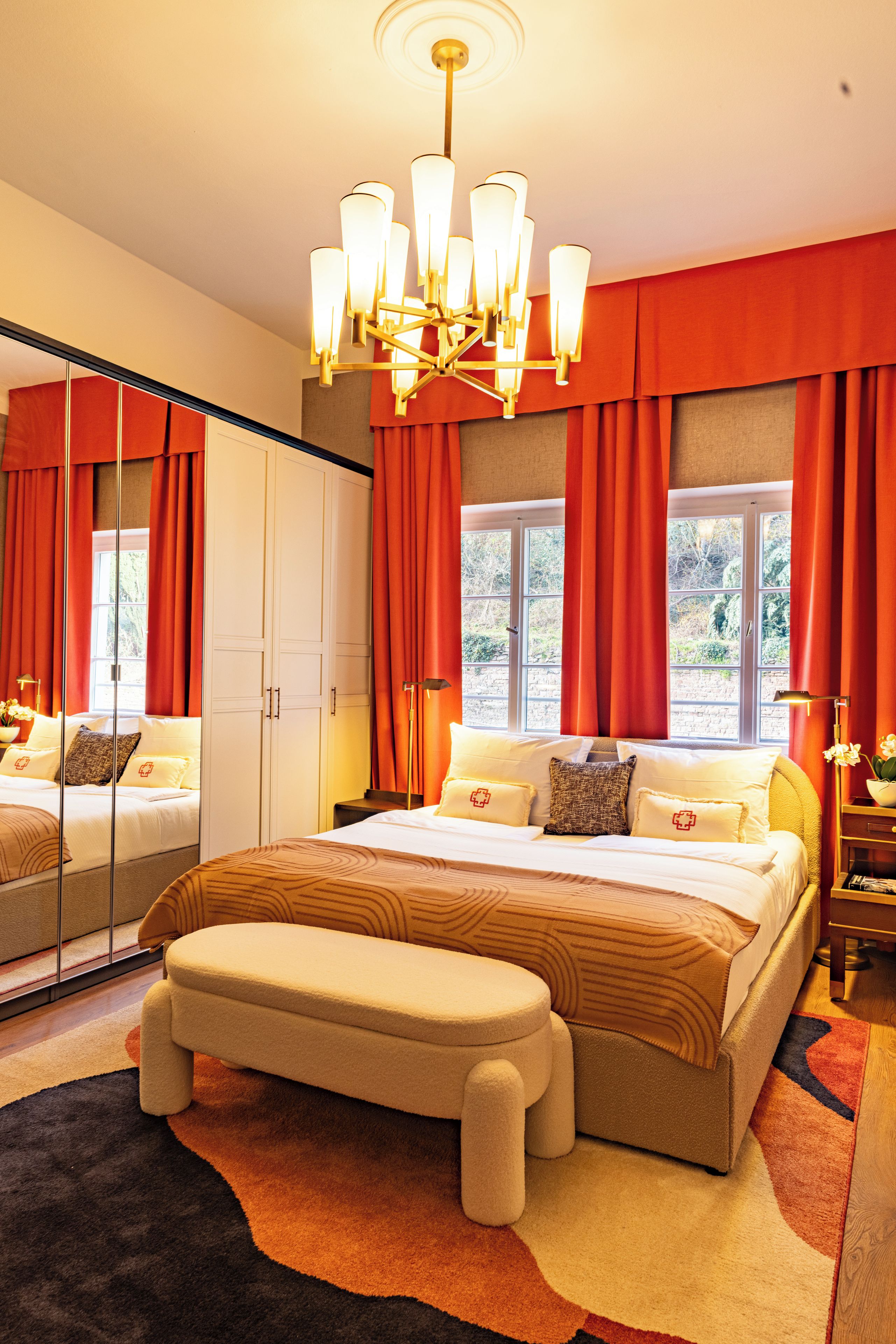A bedroom with a large bed, a bench, a wardrobe, and a mirror.