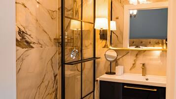 A modern bathroom with a glass-enclosed shower, marble walls, a vanity with a mirror, and a chandelier.