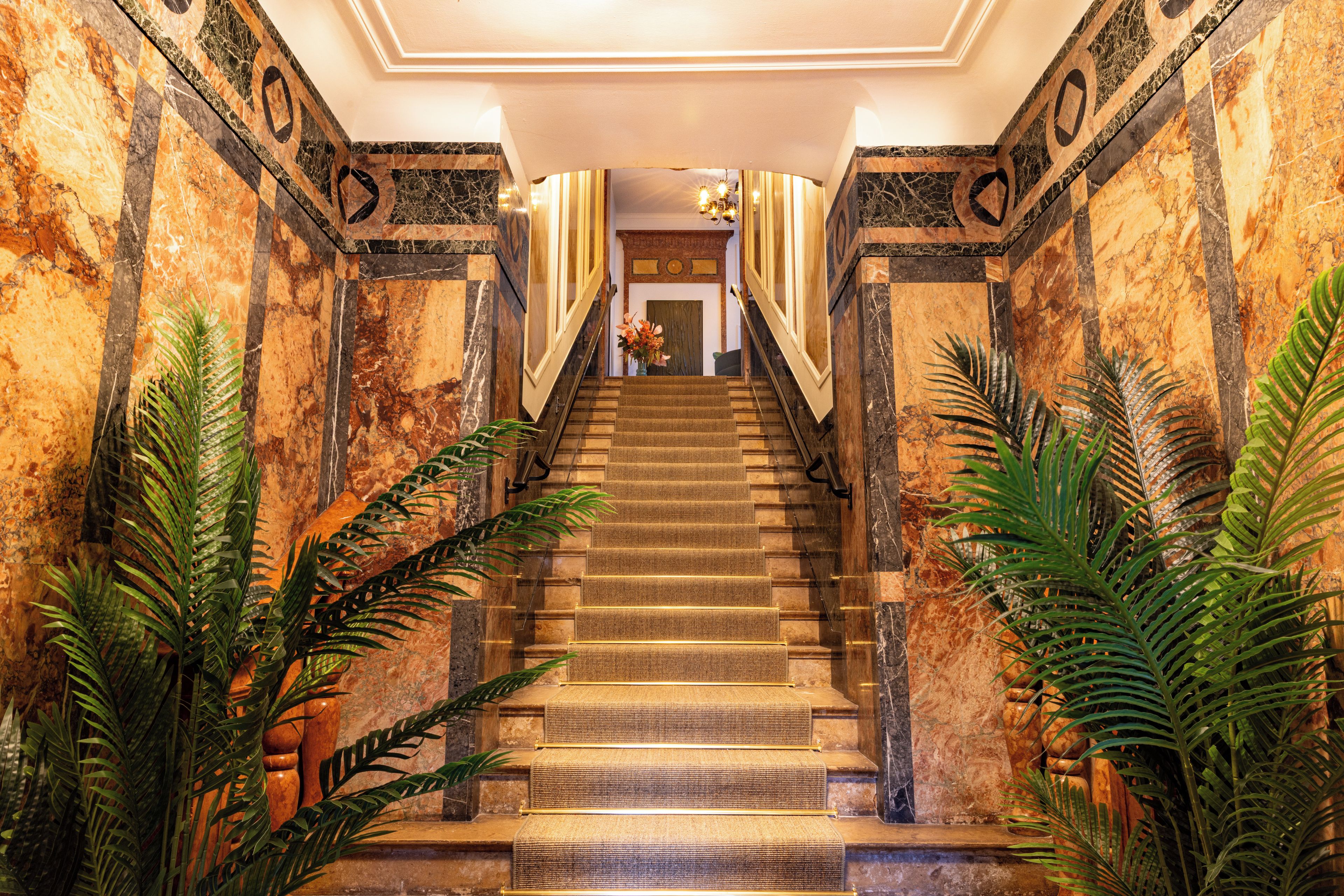 A grand staircase with marble walls and a handrail, leading to a door at the top.