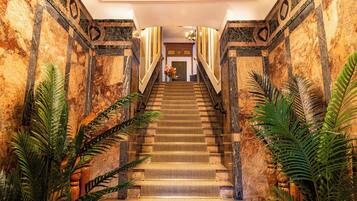 A grand staircase with marble walls and a handrail, leading to a door at the top.