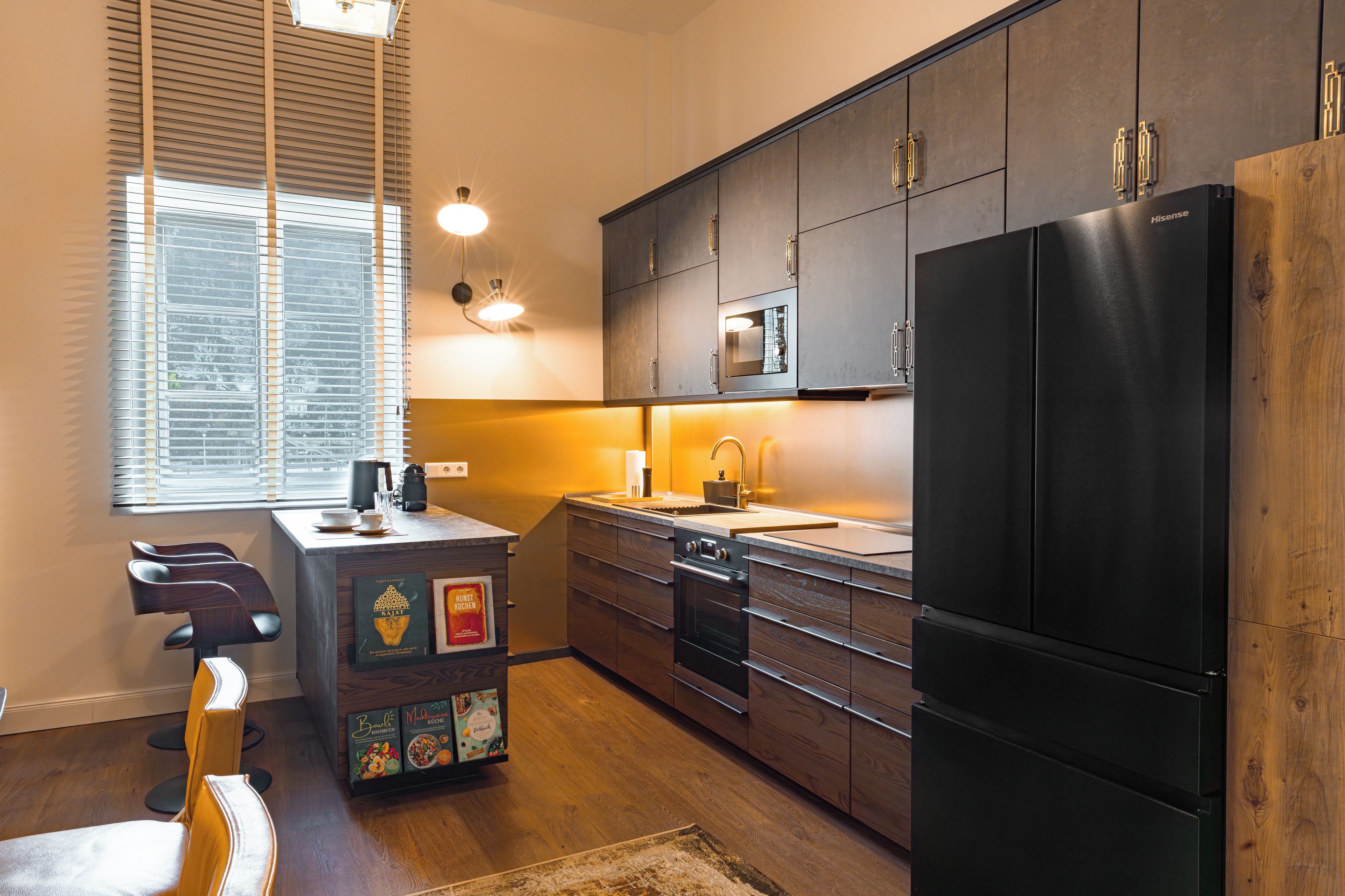 Une cuisine moderne avec des meubles de couleur sombre, un réfrigérateur noir et une fenêtre équipée de stores.