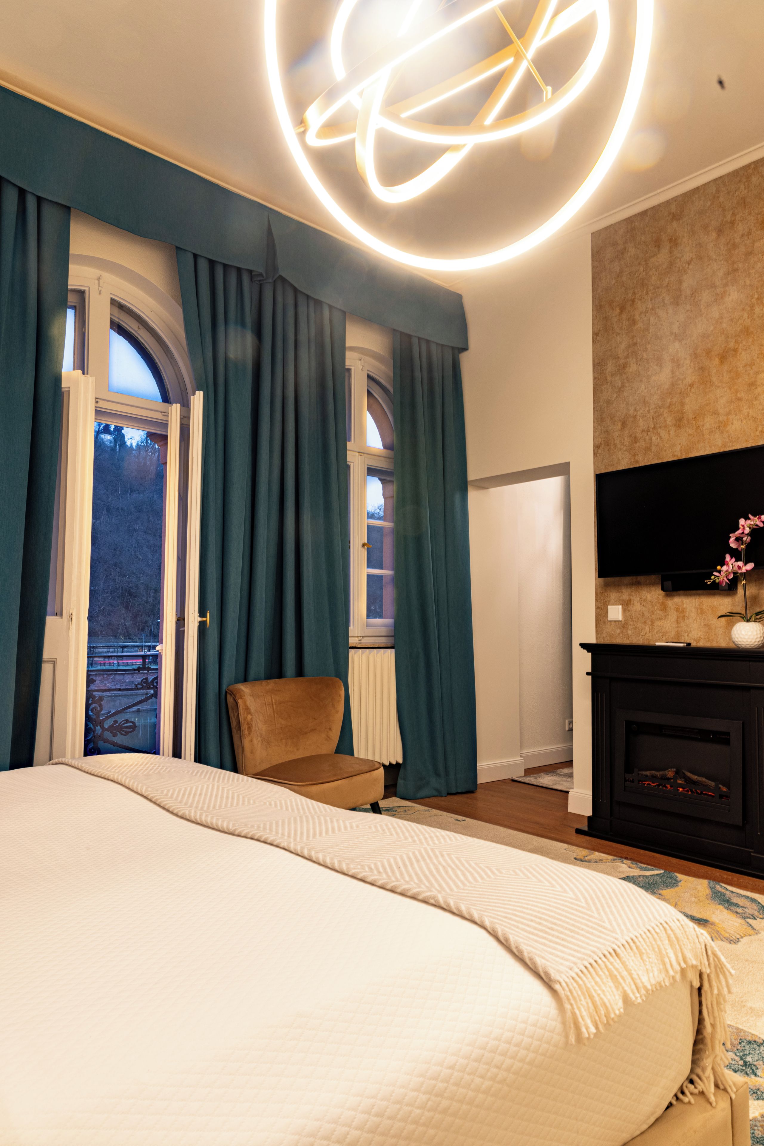 A bedroom with a large bed, a chair, a fireplace, and a TV mounted on the wall.