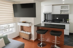 Eine moderne Küche mit Flachbildfernseher, zwei Barhocker und einem eingebauten Backofen.