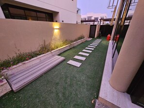 A paved pathway leading to a building entrance, with a wall on one side and a small garden area with stepping stones. - Spacious 4-bedroom townhome in Damac hills 2 in enjoyable Dubai (Dubai)
