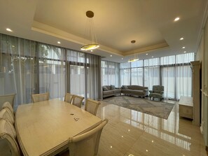 A spacious living area with a dining table, sofas, and a large window with sheer curtains. - Spacious 4-bedroom townhome in Damac hills 2 in enjoyable Dubai (Dubai)