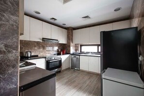 A compact kitchen with a stove, oven, and refrigerator, featuring a marble backsplash and wooden flooring. - Spacious 4-bedroom townhome in Damac hills 2 in enjoyable Dubai (Dubai)