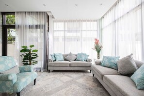 Ein modernes Wohnzimmer mit einem grauen Sofa, passenden Sessel und transparenten Vorhängen.