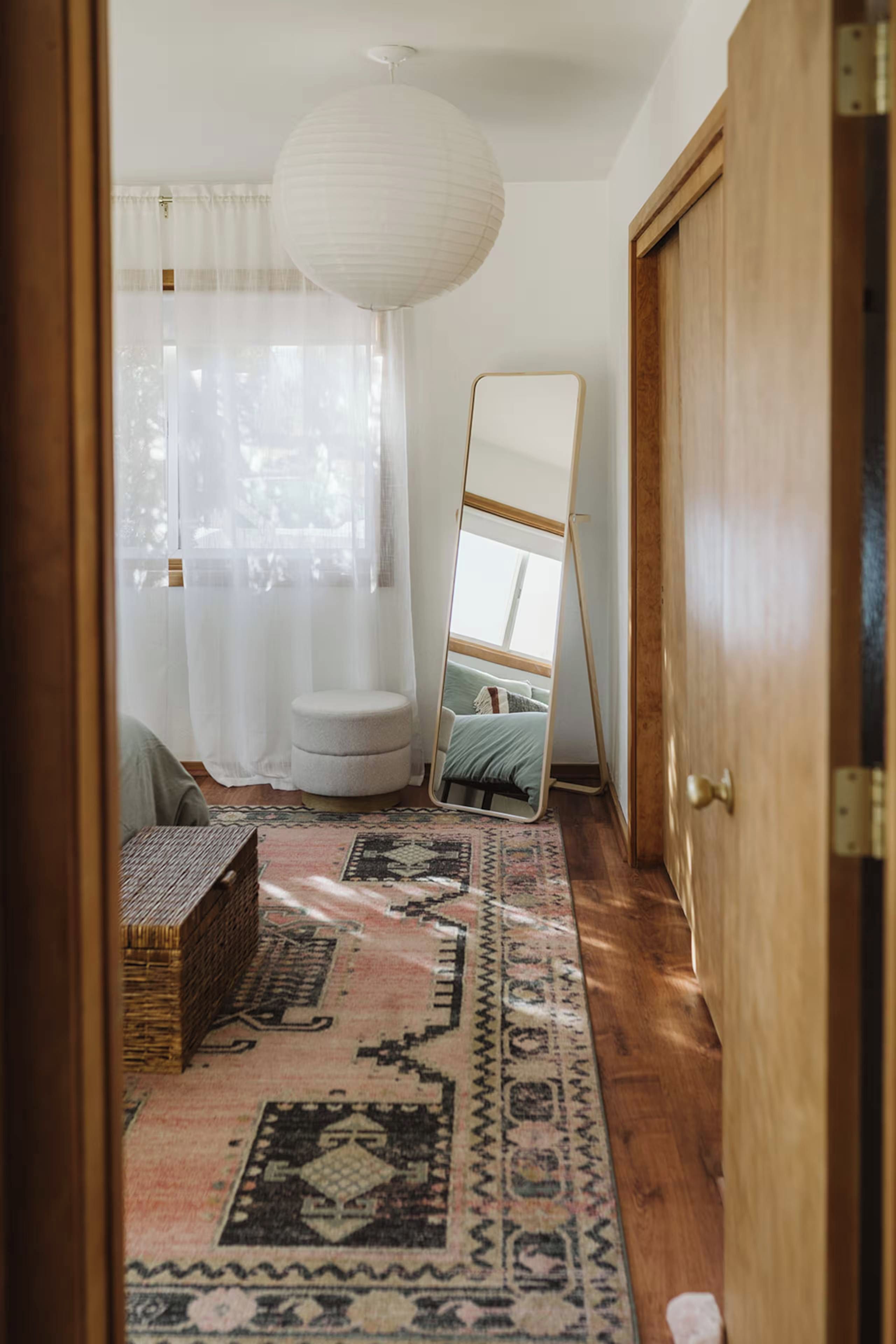 A room with a large mirror leaning against a wall, a wooden door, and a patterned rug on the floor.