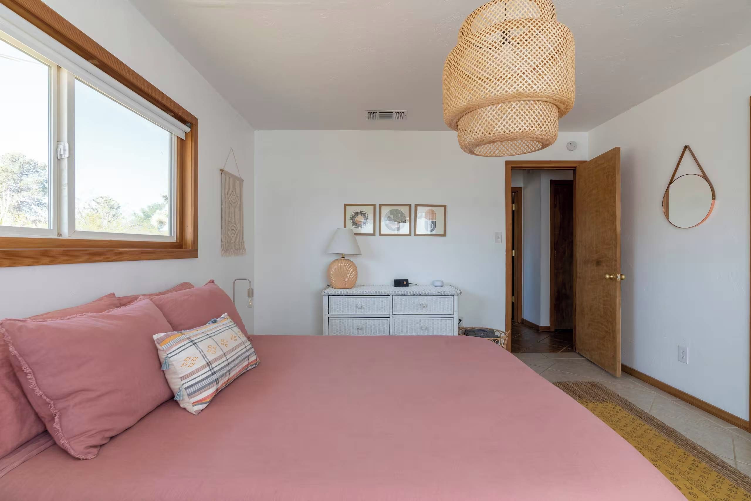 A bedroom with a large bed, a dresser, a hanging light fixture, and a window.