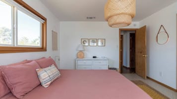 A bedroom with a large bed, a dresser, a hanging light fixture, and a window.