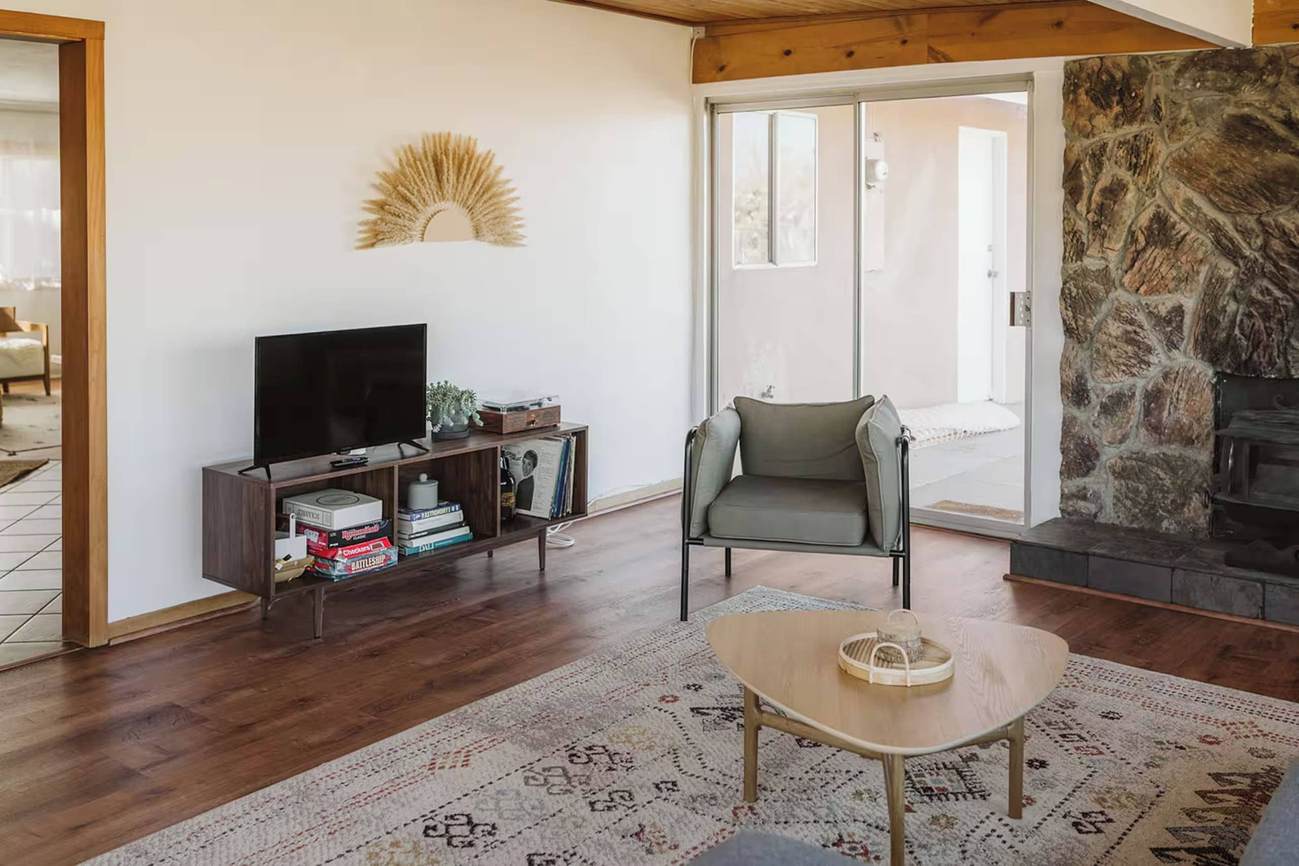 Een woonkamer met een flatscreen televisie, een boekenkast, een stenen openhaard en een vloerkleed met een patroon.