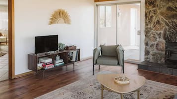 Een woonkamer met een flatscreen televisie, een boekenkast, een stenen openhaard en een vloerkleed met een patroon.