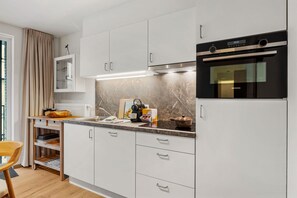 Una cocina moderna con armarios blancos, horno empotrado y encimera con cafetera y hervidor.