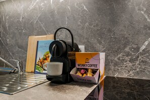 Una encimera de cocina con una cafetera, una taza, un libro de cocina y una caja de cápsulas de café.