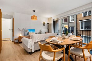 Ein modernes Schlafzimmer mit Bett, Nachttischen, einer Nachttischlampe, einem großen Fenster und einem Balkon mit Essplatz.