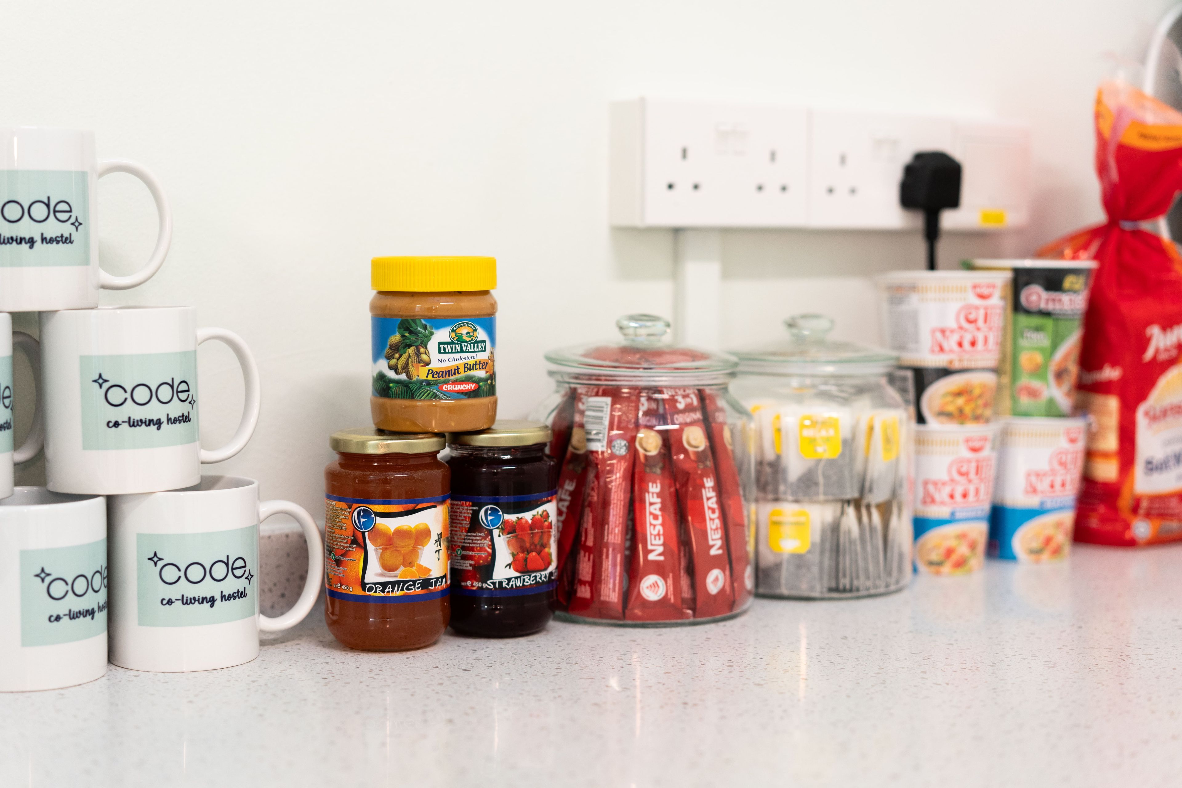 A kitchen counter with various food items and a stack of white mugs with text.
