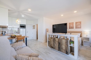 A modern living room with a sofa, a TV, and a dining area with a table and chairs. - Apartment 'White Studio - Garden & Sea View' with balcony, Wi-Fi and air conditioning (Albufeira)