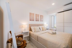 A bedroom with a bed, bedside lamps, a nightstand, a wooden chair, and wall art. - Apartment 'White Studio - Garden & Sea View' with balcony, Wi-Fi and air conditioning (Albufeira)