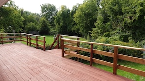 Een houten terras met een balustrade, met uitzicht op een gazon met bomen.