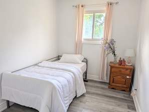 Ein Schlafzimmer mit einem Einzelbett, einem Nachttisch mit Lampe und einem Fenster mit Vorhängen.