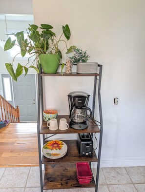Ein Holzregal mit einer Kaffeemaschine, Tassen, einem Teller mit floralem Dekor und einer roten Ablagefläche.