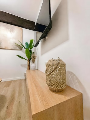 Una mesa de madera con una cesta tejida, una planta en maceta y un estante fijado a la pared.