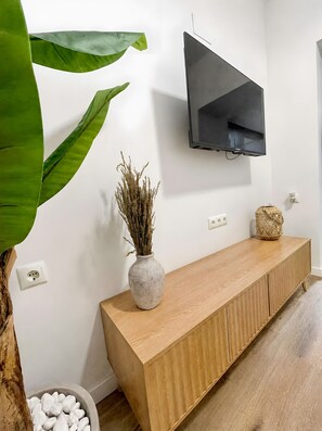 Un salon moderne avec une console en bois, un téléviseur fixé au mur, un vase contenant des plantes séchées et une grande plante verte.