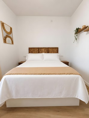 Una cama bien hecha con cabecera de madera, ropa de cama blanca y una manta color beige.