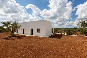 A modern white building with a flat roof, surrounded by a dry, brown landscape with sparse trees. - Casa tra gli Ulivi by Perle di Puglia (Ostuni)