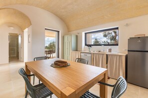 A modern kitchen with a wooden dining table, chairs, a built-in oven, and a view of the outdoors. - Casa tra gli Ulivi by Perle di Puglia (Ostuni)
