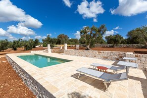 A swimming pool with a stone deck, surrounded by olive trees and a stone wall. - Casa tra gli Ulivi by Perle di Puglia (Ostuni)