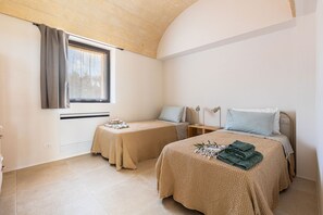 A bedroom with two beds, a window with curtains, a bedside table with a lamp, and a wall-mounted heater. - Casa tra gli Ulivi by Perle di Puglia (Ostuni)