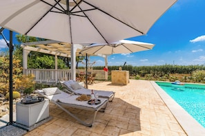 A covered outdoor area with lounge chairs, a table with drinks, and a pool. - Villa Carolyta by BarbarHouse (Francavilla Fontana)