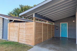 Un edifici modern amb un pati cobert, una porta blava i una tanca de fusta.