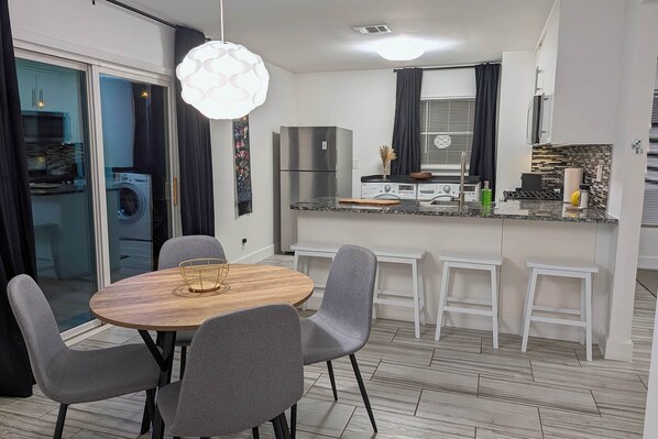 A modern kitchen with a refrigerator, microwave, and stove. There is a dining area with a round table and chairs. - Freshly Renovated | Newly Furnished | Game Room (Austin)