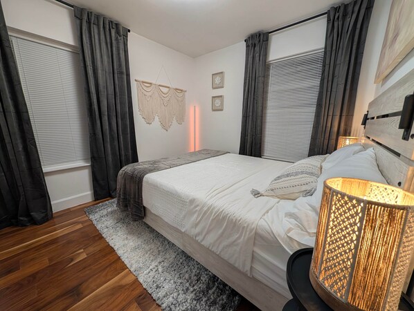 Une chambre à coucher avec un lit, une lampe de chevet, un tapis gris et des rideaux.