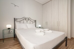 Ein ordentlich bezogenes Bett mit weißen Leinen, zwei Nachttische mit Lampen und ein zweitüriger Kleiderschrank.