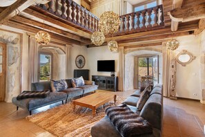 A spacious living room with a high ceiling, wooden beams, a large sofa set, a wooden coffee table, and a television. - Château 'Le Chateau Des Girards' authentically renovated (Lans-en-Vercors)
